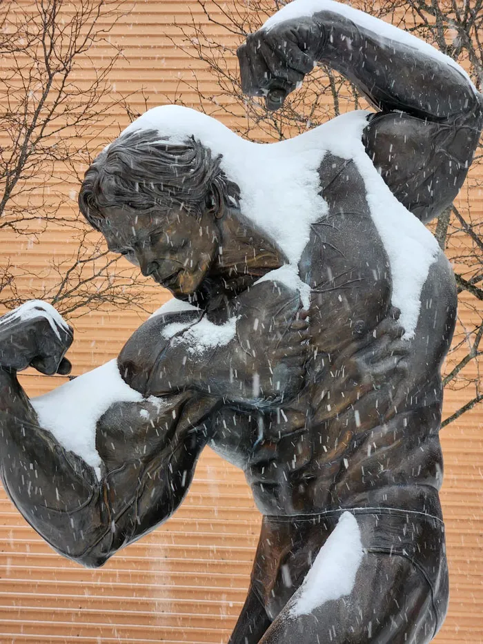 Bronze statue of a muscular man covered in snow during a heavy snowstorm in the U.S. winter.