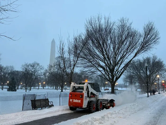 Snowstorm hitting the U.S. with a Bobcat clearing snow on a path near the Washington Monument on a winter day.