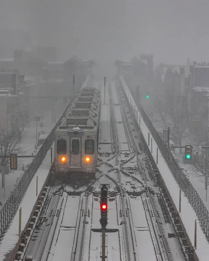 Train on snowy tracks during a heavy snowstorm in the U.S. with low visibility and snow-covered cityscape in the background