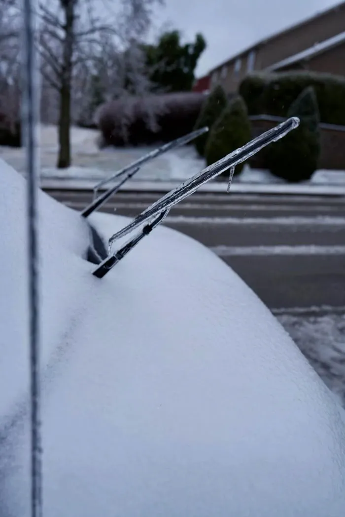 Car windshield wipers covered in ice after a heavy snowstorm in the U.S. with snow blanketing the surroundings.