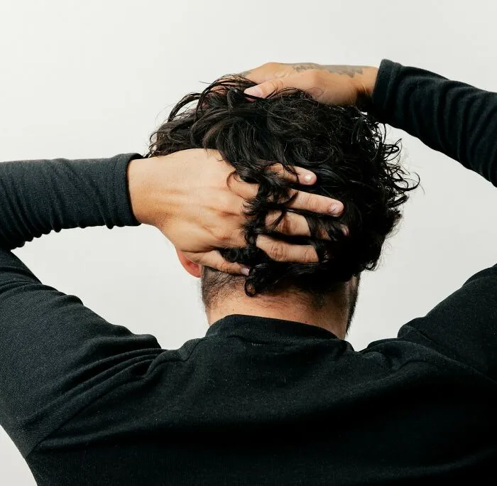 Person with curly hair holding their head, illustrating cultural differences shared by 35 people about normal versus offensive behaviors.