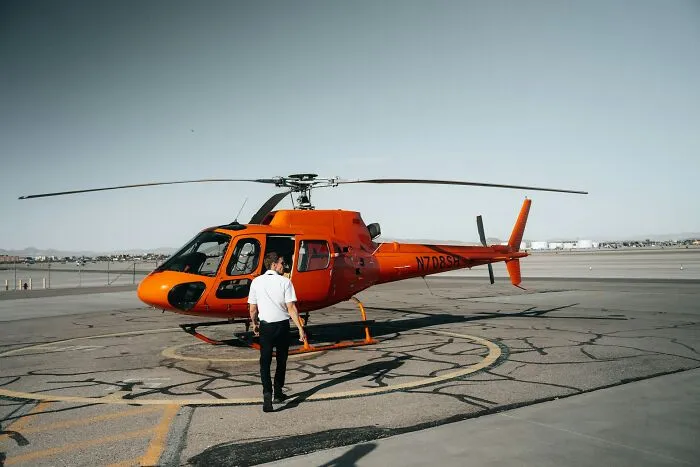 A man walking toward a bright orange helicopter on an airport runway showing how far from reality rich people can be.