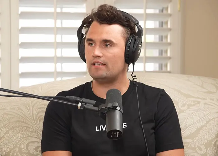 Man wearing headphones and a black shirt speaking into a microphone during a podcast about celebrity passings.