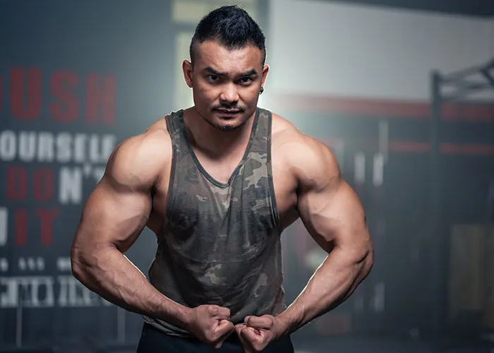 Muscular man in camo tank top flexing arms in gym, illustrating strength and determination after petty ex revenge.