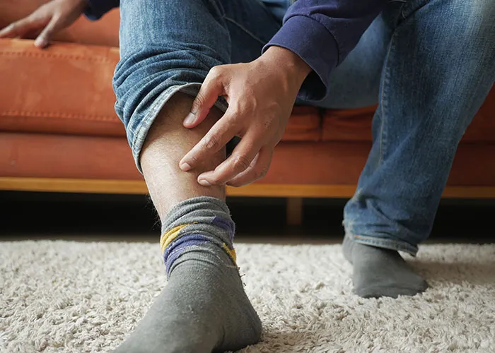 Person sitting on a couch, pulling up pant leg to reveal a sock, illustrating pettiest ways people got back at an ex.