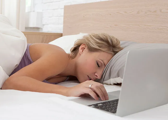 Woman lying face down on bed using a laptop, illustrating exhaustion after getting back at an ex in the pettiest way possible.