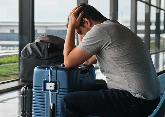Man sitting at airport with head in hands, showing frustration after petty revenge on an ex in a tense moment.