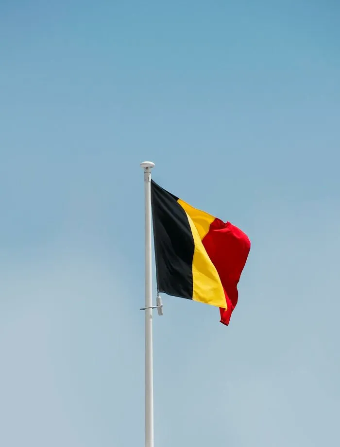 Belgium flag waving on flagpole against a clear blue sky representing local inside jokes and culture.