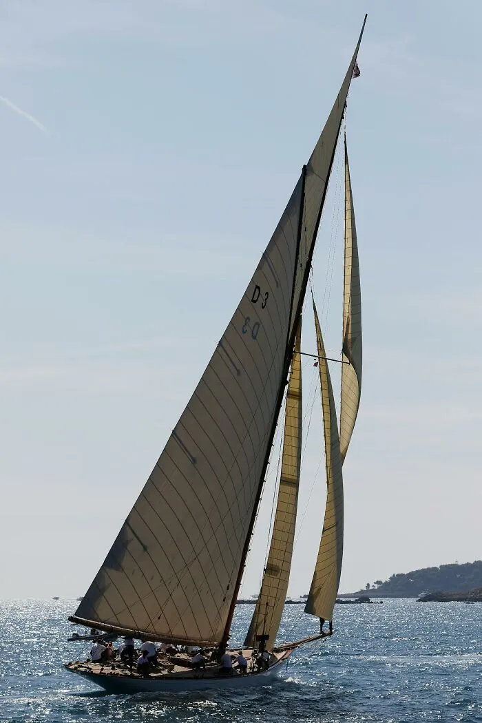 A luxury sailboat with large sails gliding on a sunny sea, illustrating rich people far from reality lifestyle.