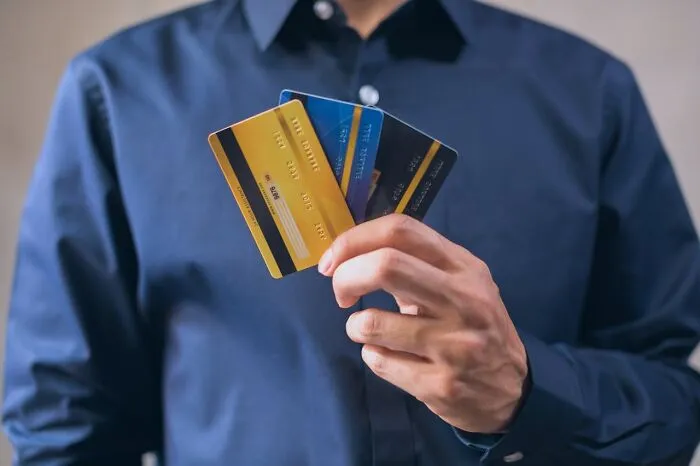 Person in blue shirt holding multiple credit cards, illustrating how rich people show disconnect from reality.
