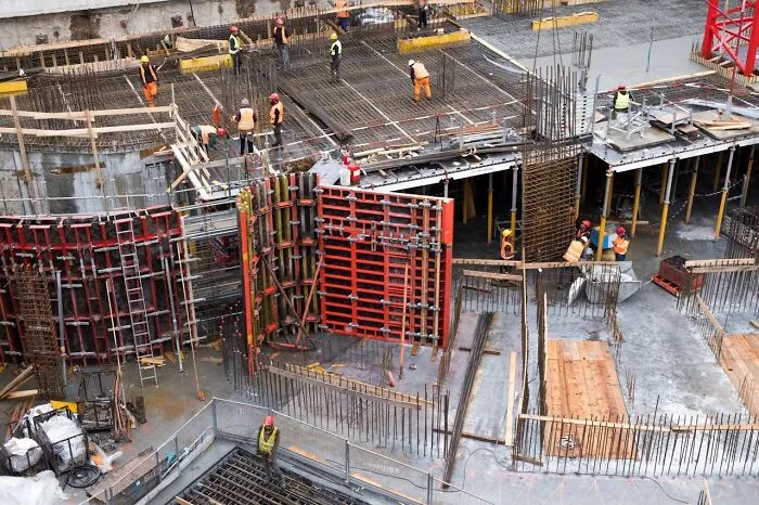 Construction workers actively building a concrete structure at a large urban site, illustrating local inside jokes about teamwork.