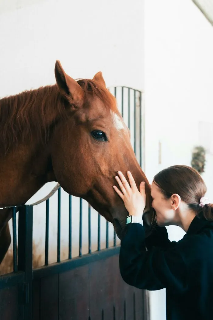 Woman gently touching a horse's face inside stable, illustrating how rich people show how far from reality they are.