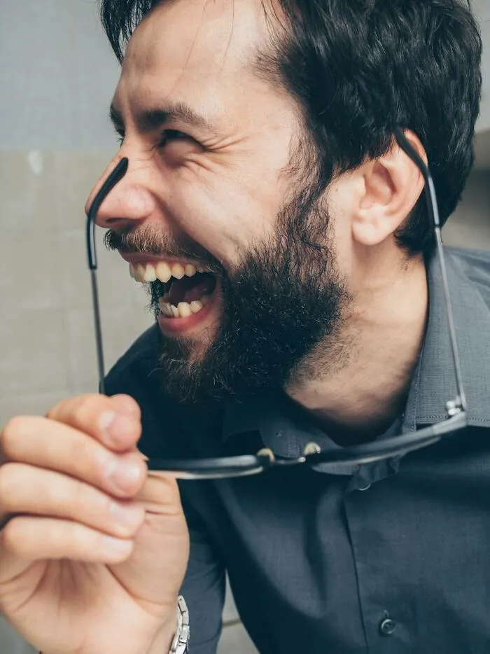 Bearded man laughing while holding glasses, captured in a candid moment reflecting local inside jokes and humor.