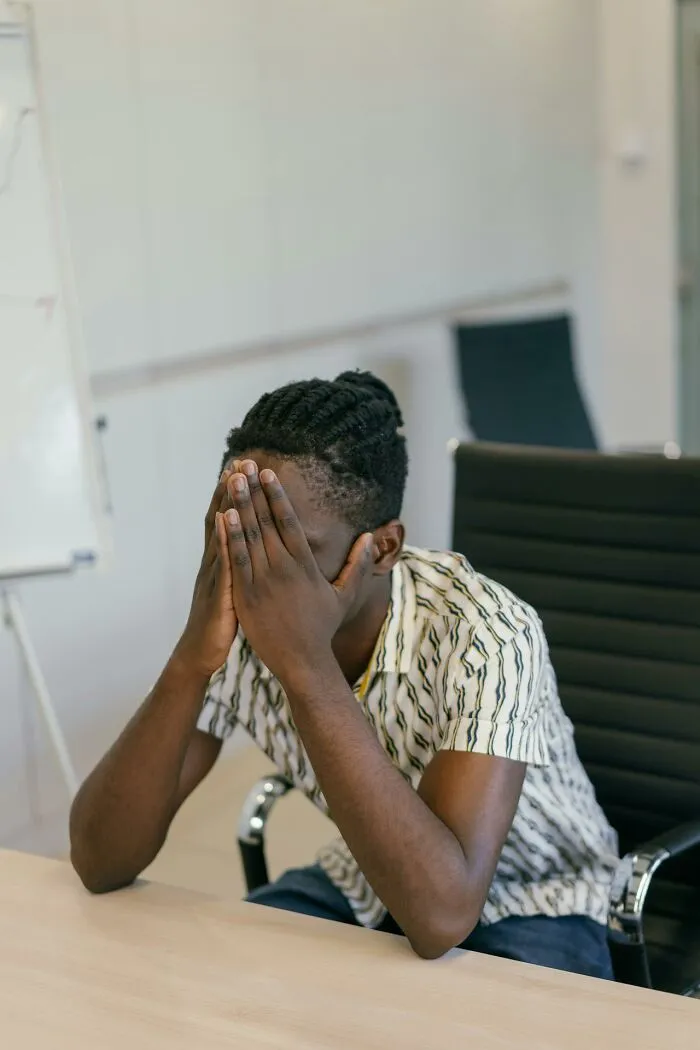 Young man covering his face in an office, stressed, evoking It Rained Frogs story