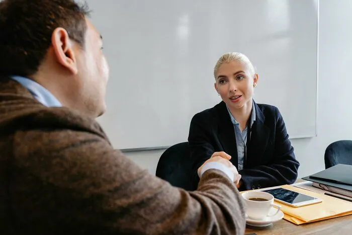 Two coworkers shaking hands across a table during a meeting illustrating worst coworkers ever workplace interactions.
