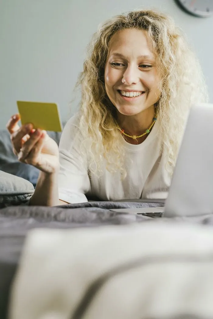 Smiling woman on bed holding a card beside laptop, illustrating creepiest displays of intelligence online
