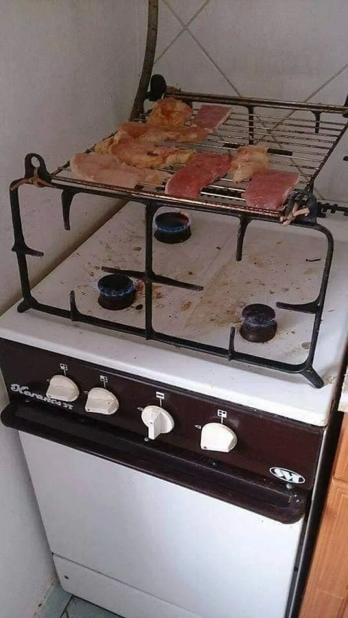 Old stove with raw meat slices cooking on a metal rack above the burners, capturing Eastern European experience humor.