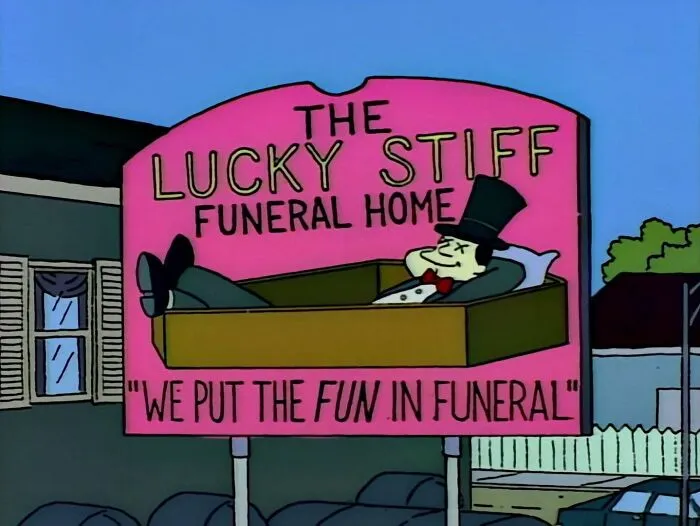 The Simpsons scene showing a humorous Lucky Stiff Funeral Home sign with a man relaxing in a coffin.