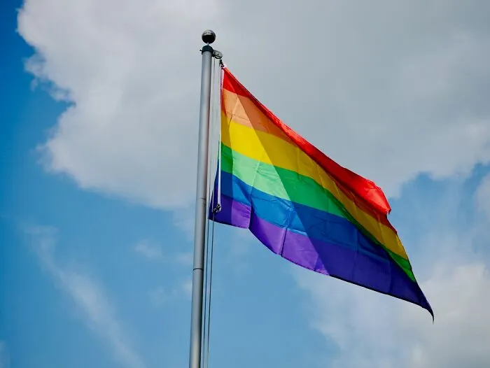 Rainbow pride flag flying on a pole against a cloudy sky representing cultural differences and offensive gestures worldwide.