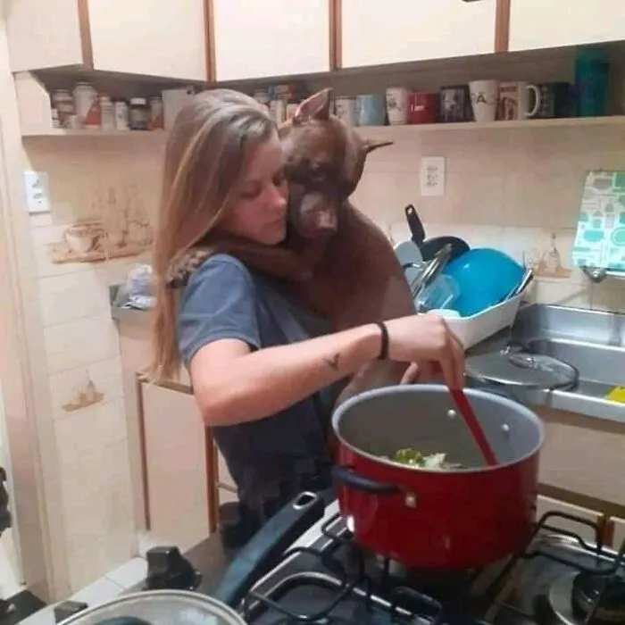 Woman holding and hugging her dog while cooking in the kitchen, showing unexpectedly beautiful bonds between humans and animals.