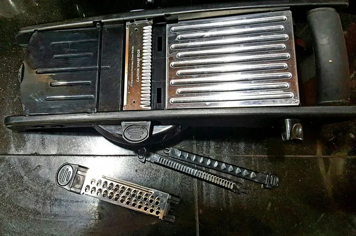 Mandoline slicer with interchangeable blades on a black surface highlighting sharp kitchen tools healthcare workers avoid using.