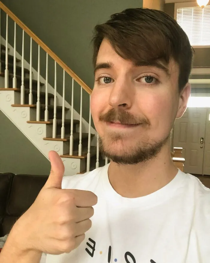 Young man giving a thumbs up in a home setting with stairs in the background, unrelated to coffin birth or dark scary facts.