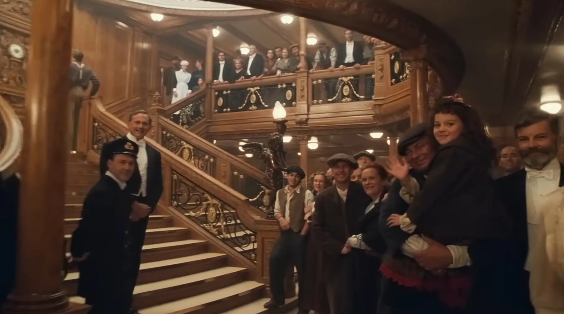 Crowd gathered on grand staircase in film final scene, dressed in early 20th century attire, smiling and waving.