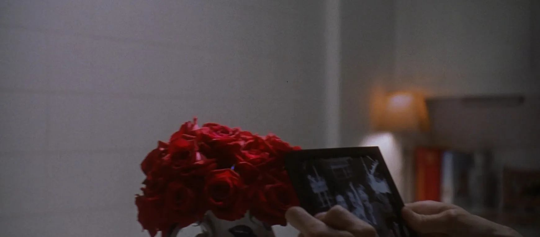 Close-up of hands holding a photo frame next to a bouquet of red roses in a movie final scenes setting.