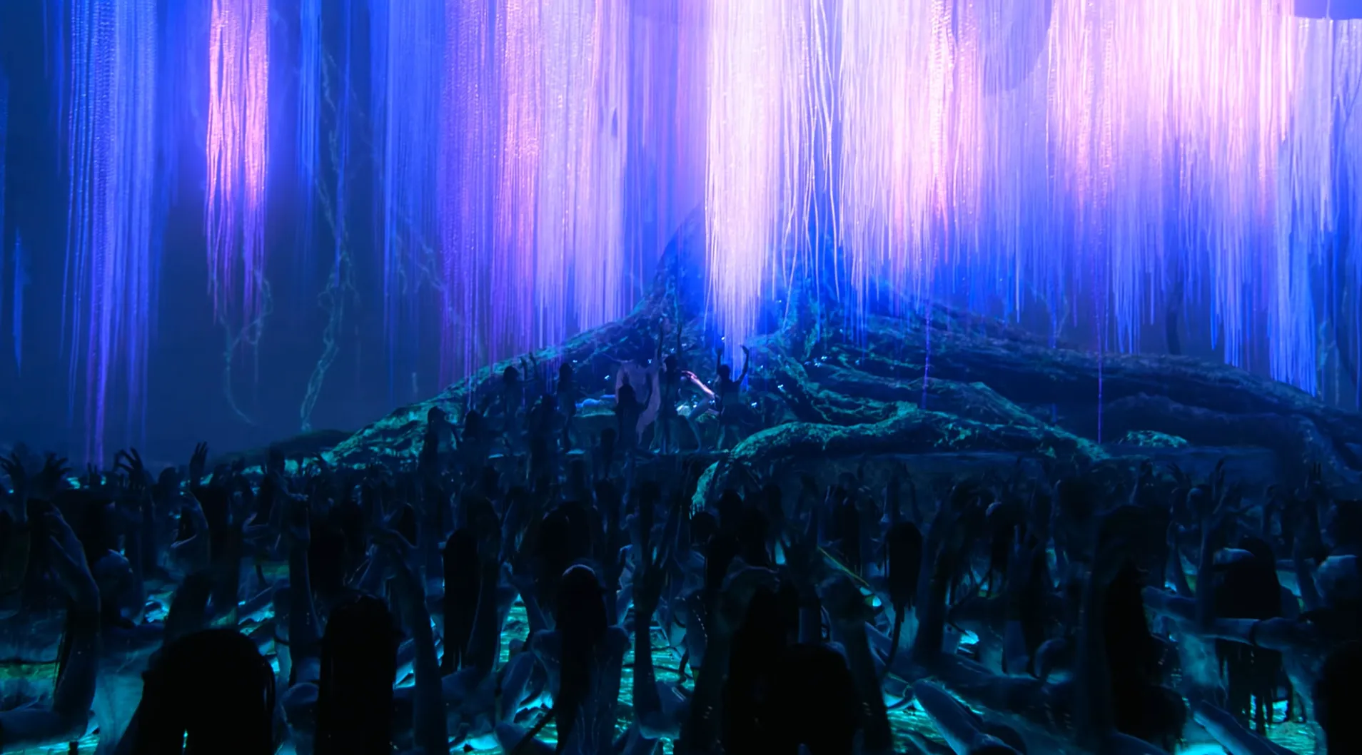 Final scene from a movie with glowing blue hanging lights and a large group of people gathered under a mystical tree.