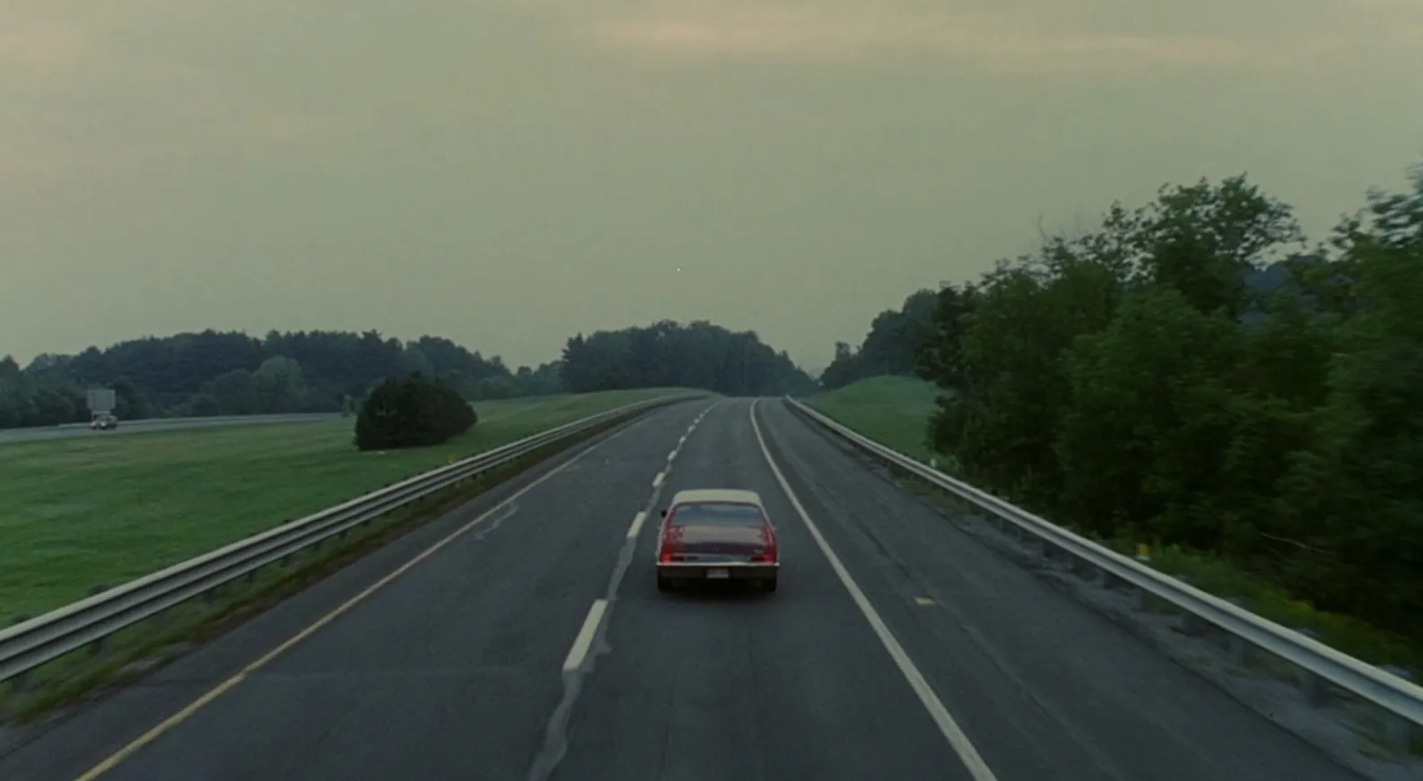Car driving alone on an empty highway surrounded by trees in a quiet setting, captured in a movie final scenes part 3.