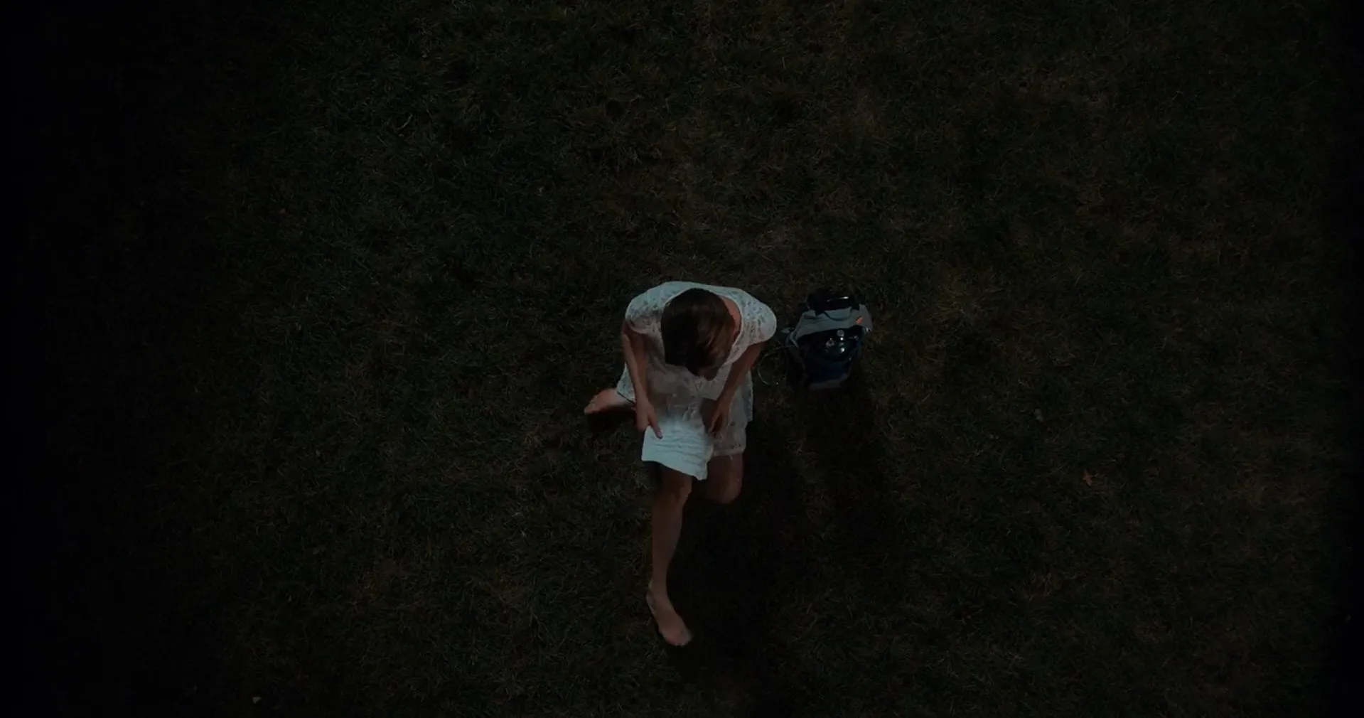 Woman in white dress sitting on grass at night reading a letter in a movie final scene from Part 3