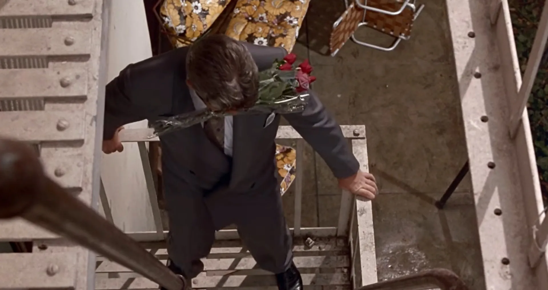 Man in suit holding roses, walking on metal stairs in a tense moment from movie final scenes part 3