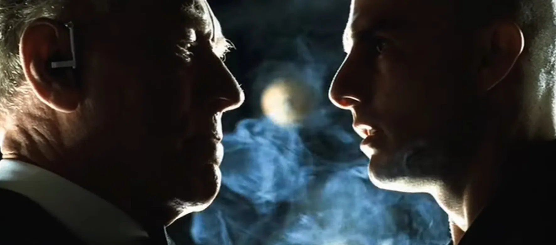 Two men face each other closely with smoke in the background in a dramatic movie final scenes moment.