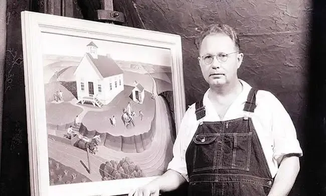 Black and white photo of Grant Wood standing beside his painting depicting a farmer and daughter in front of a rural home.