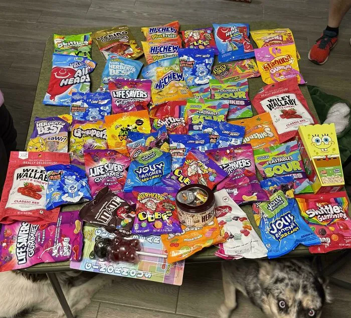 A large haul of various candy bags and boxes spread across a table, a sweet treasure found through dumpster diving.