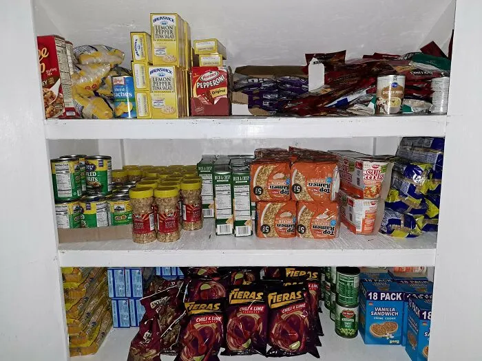 Shelves stocked with numerous boxes of ramen, canned goods, and snacks, all from dumpster diving.
