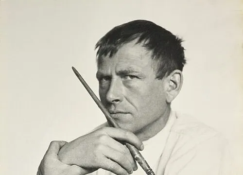 Black and white portrait of German artist Otto Dix holding a paintbrush, looking thoughtfully into the distance.