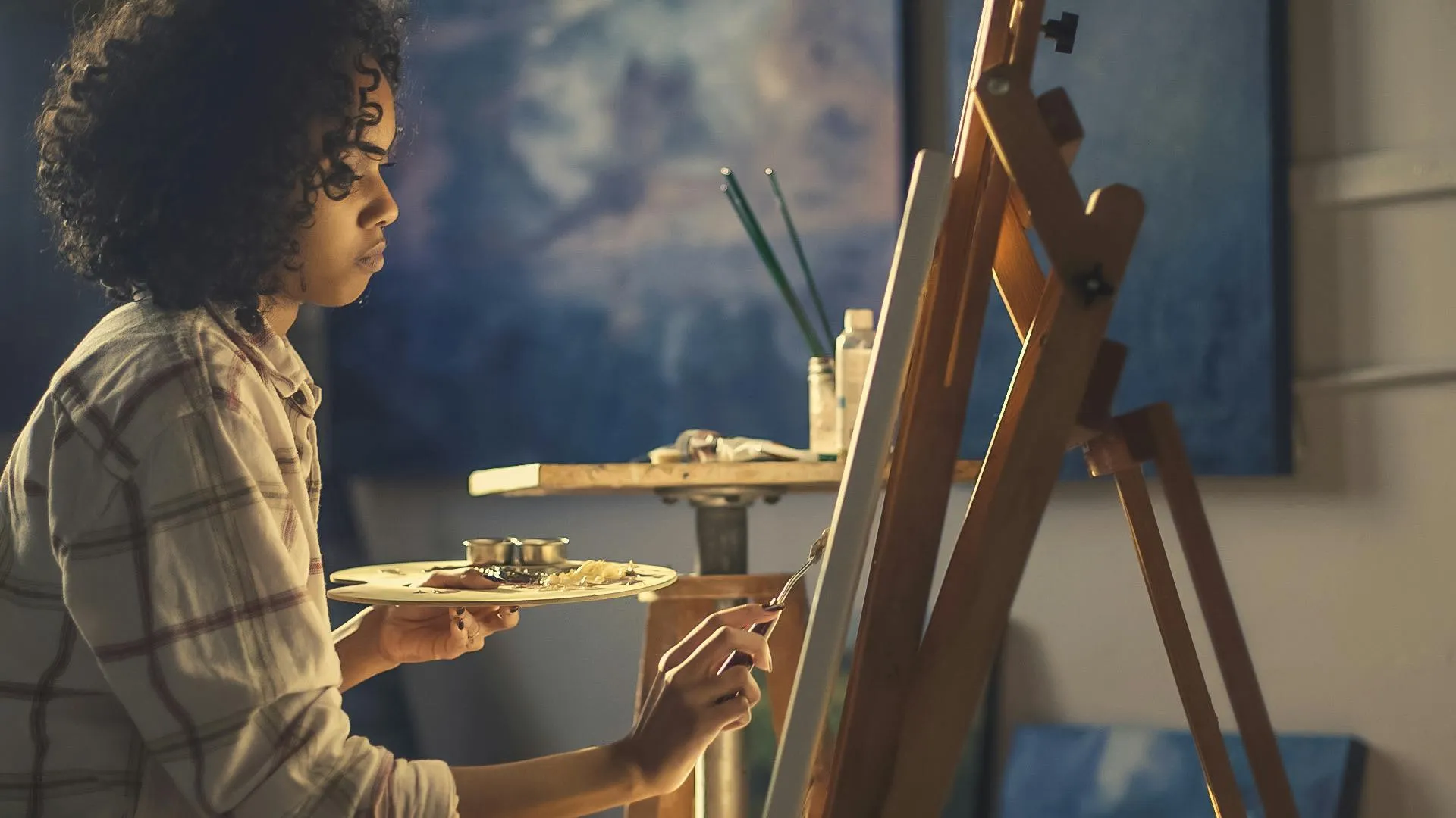 Woman artist painting on canvas in studio focused on creating a self-portrait using palette and brush.