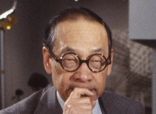 Portrait of architect and artist I. M. Pei wearing round glasses and a suit, thoughtful in an indoor setting.