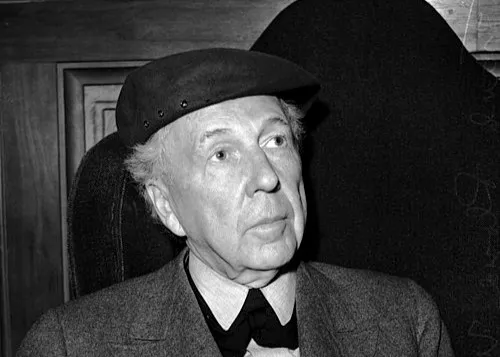 Frank Lloyd Wright wearing a hat and suit, sitting and looking thoughtfully in an indoor setting.