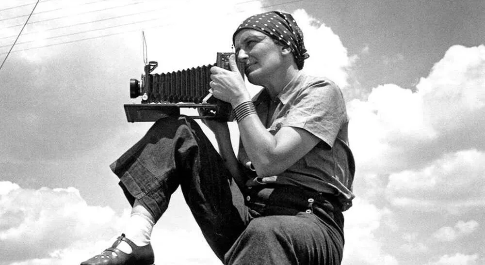 Photographer Dorothea Lange using vintage camera outdoors, capturing an iconic Great Depression photograph.