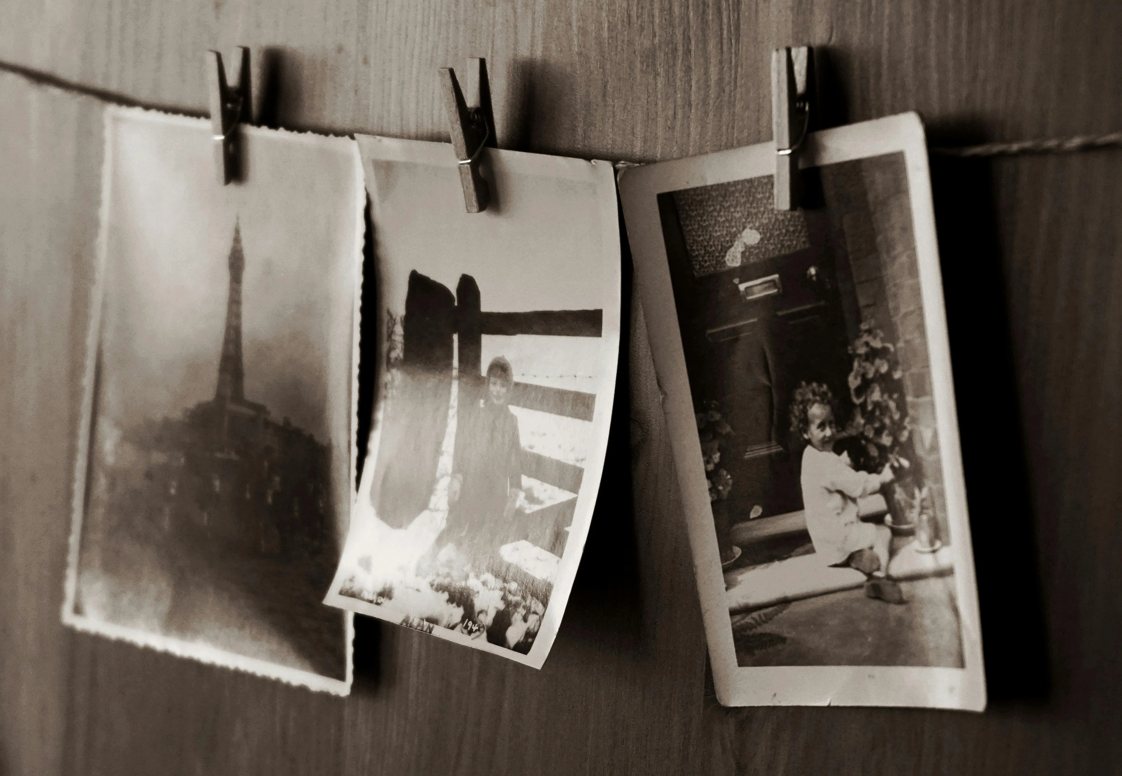 Vintage photographs hanging on a string with clips showing different scenes and varying light or dark photographic tones.
