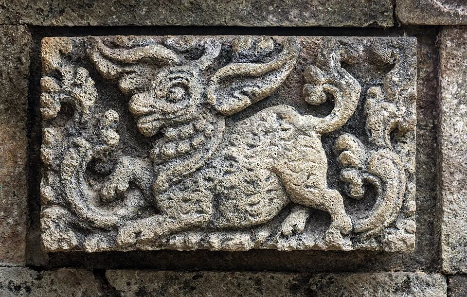 Stone relief sculpture depicting a fantasy creature projecting outward from the background surface on a stone wall.