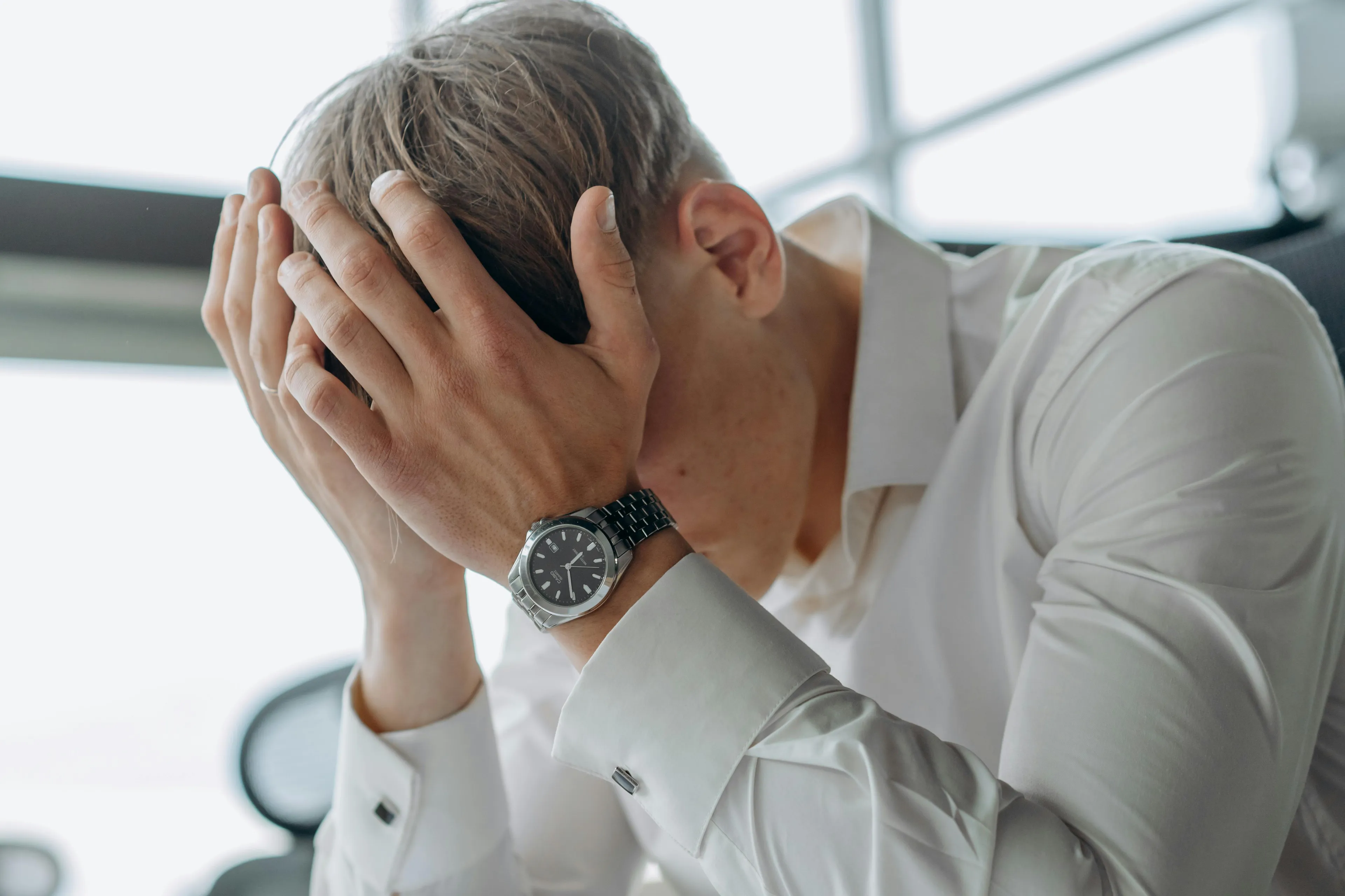 Man in white shirt with watch holding his head showing mental discomfort from conflicting beliefs concept.