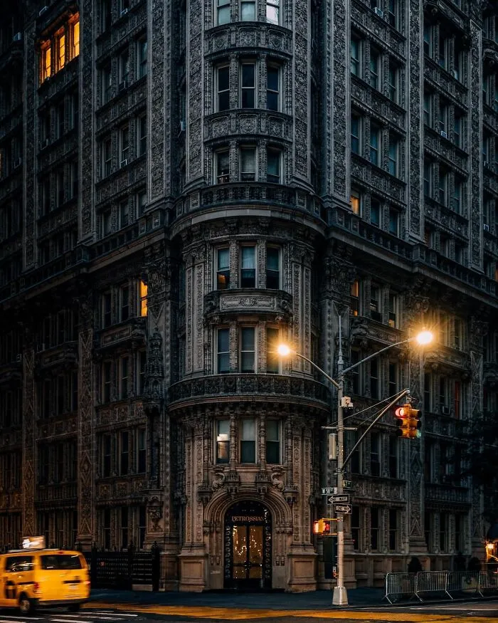 Stunning and beautiful architecture of an old, intricately detailed building at a street corner with glowing windows and streetlights.