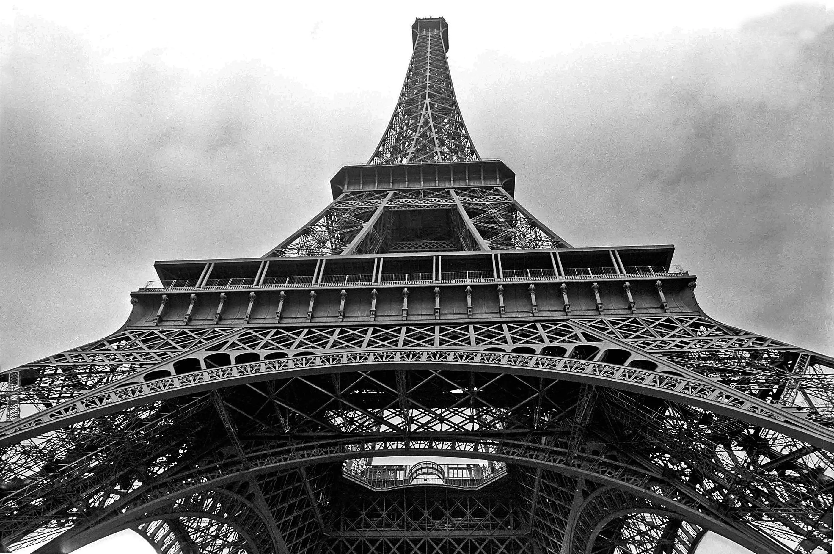 Close-up view of the Eiffel Tower structure in Paris against a cloudy sky, showing iron lattice work from below.