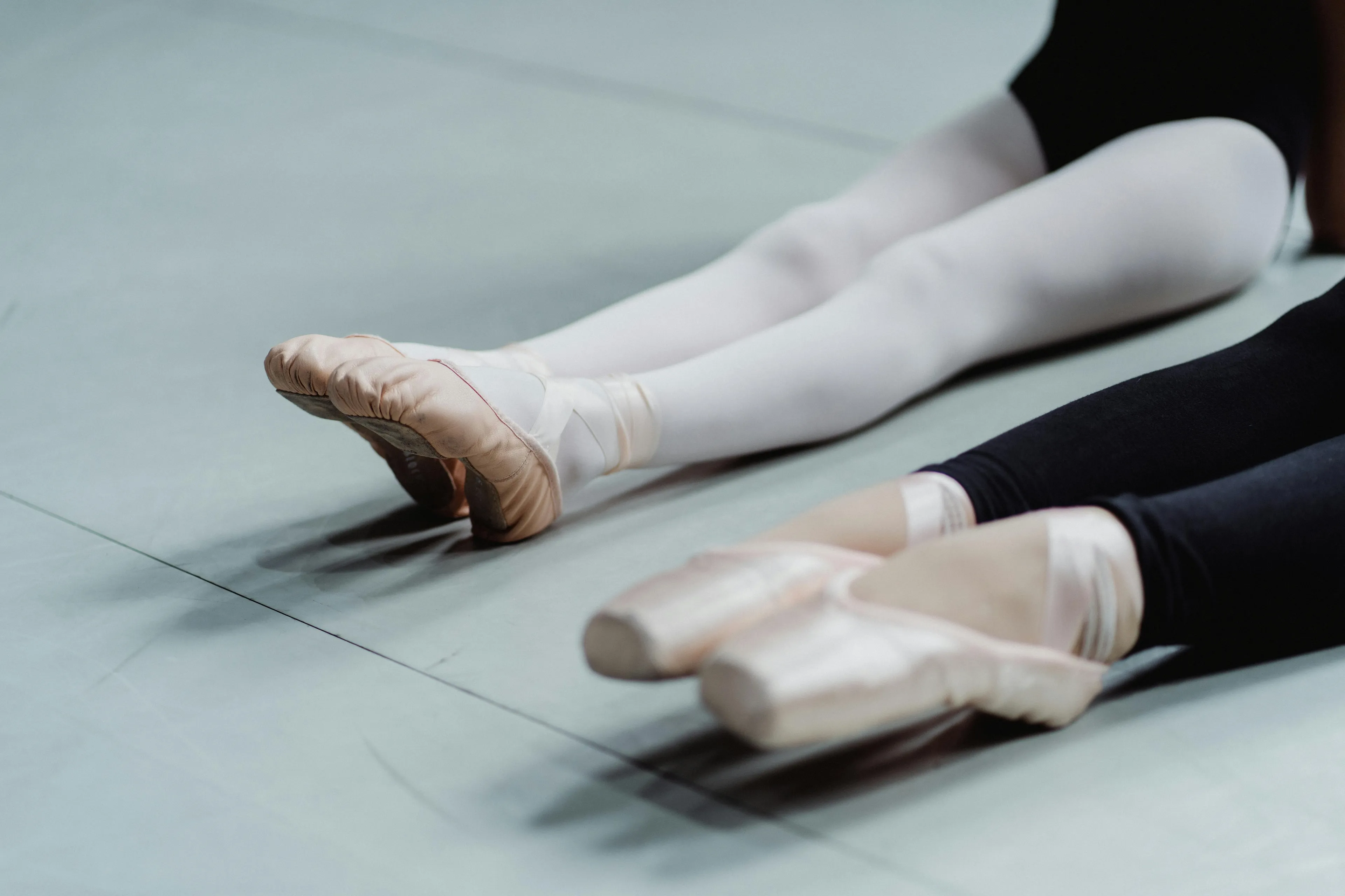 Ballet dancers wearing pointe shoes stretching legs on floor demonstrating ballet term on the toes technique.