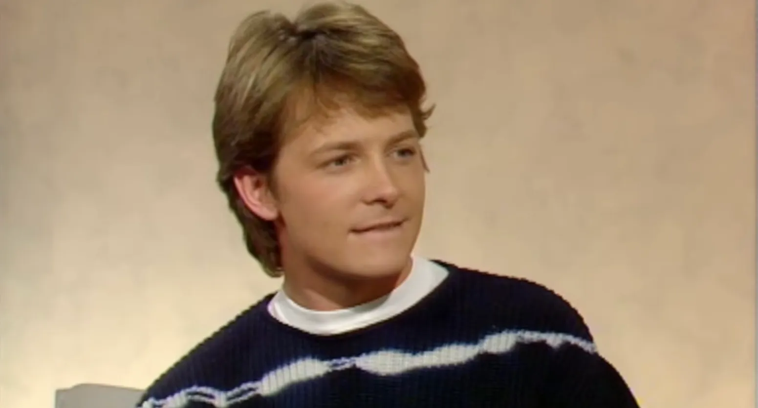 Young male actor from the 80s wearing a striped sweater, looking sideways in an interview setting about time travel in a DeLorean
