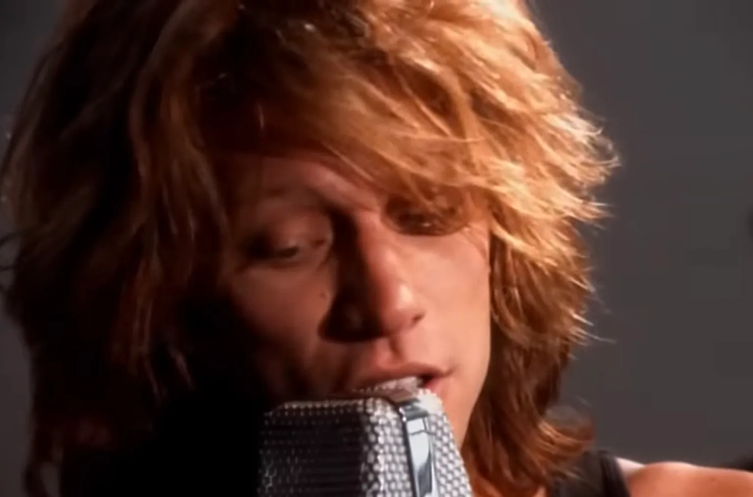 80s rock singer performing with vintage microphone, known for chart-topping anthems and iconic 80s music style.