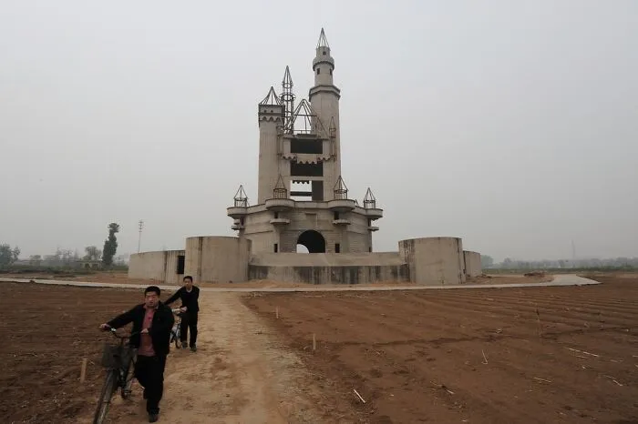 Unusual places featuring a unique, abandoned castle-like structure in a barren landscape with two people walking bikes nearby.
